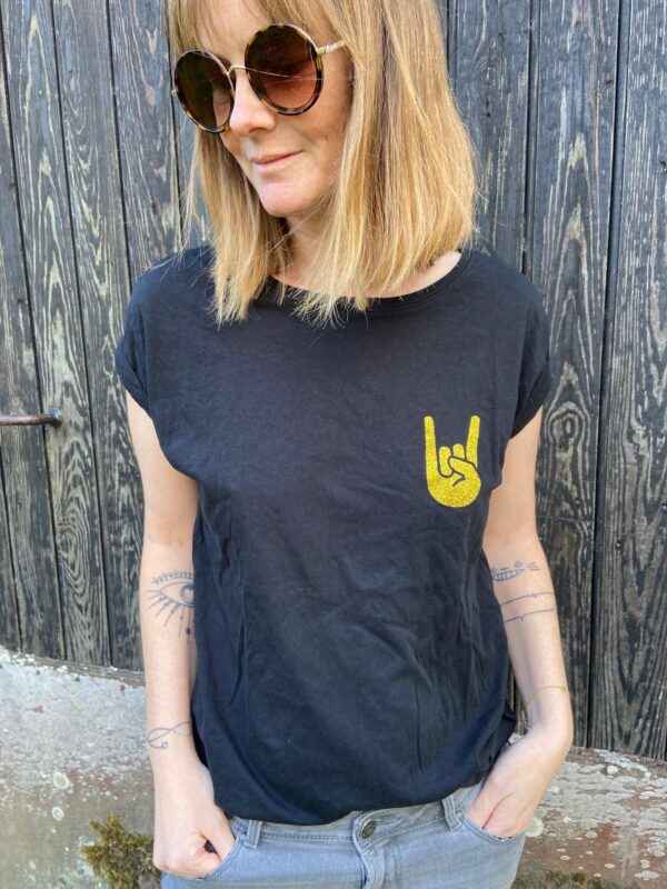 Laisse parler ton côté rock et glamour avec notre t-shirt noir Hell Yeah ! Avec son sigle pailleté doré rempli sur le cœur et son petit cœur doré discret dans la nuque, c’est bien plus qu’un simple T-shirt : c’est une déclaration de style. Conçu et personnalisé dans notre atelier entre Nantes et Clisson, il reflète l’ADN de la boutique : pièces originales, limitées et ultra-tendances.